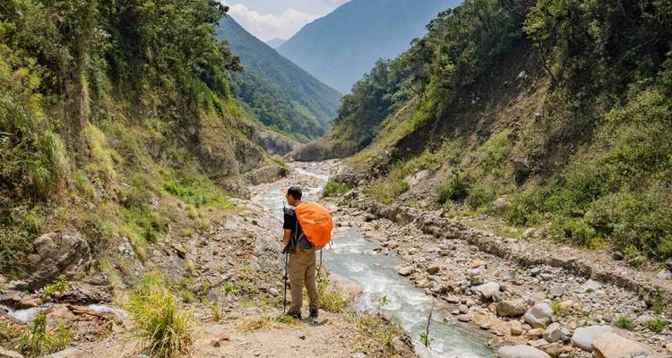 Randonneur avec sac à dos debout près d'une rivière entre les montagnes.