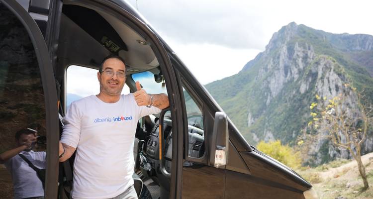 Mann posiert mit einem Lieferwagen und Bergen im Hintergrund.