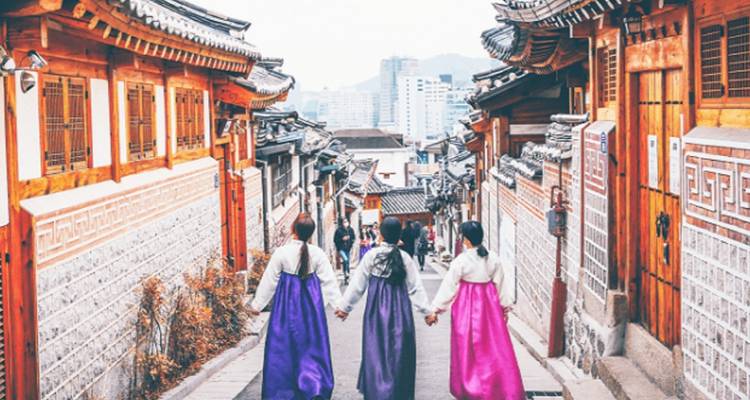 Des personnes en Hanbok traditionnel marchant dans un village coréen historique.