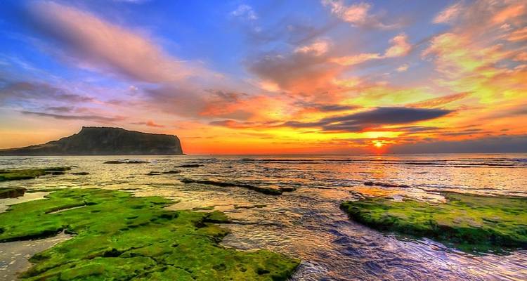 Coucher de soleil sur l'océan avec des rochers couverts de mousse et un ciel dramatique.
