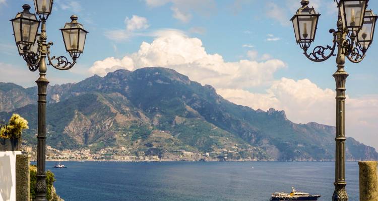 View across the Amalfi Coast framed by ornate street lamps, with mountains and boats on calm sea.