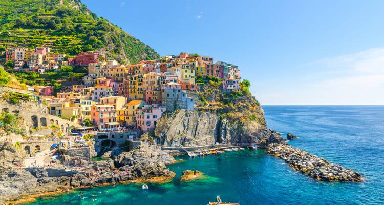 Colorful cliffside village of Manarola with turquoise water and rocky shoreline on a sunny day.