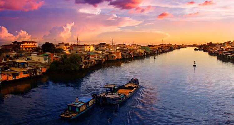 Sonnenuntergang über einem Fluss mit einem Boot, das entlangfährt, Häuser an den Ufern.
