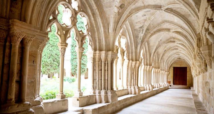 Stone cloister with arches overlooking a green courtyard.