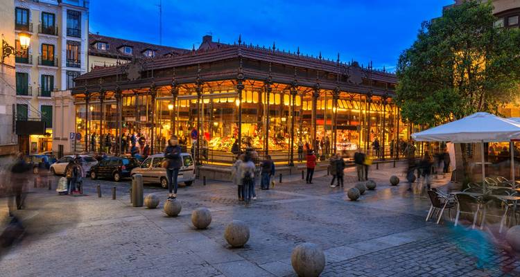 Bustling market square with glass building, illuminated at night.