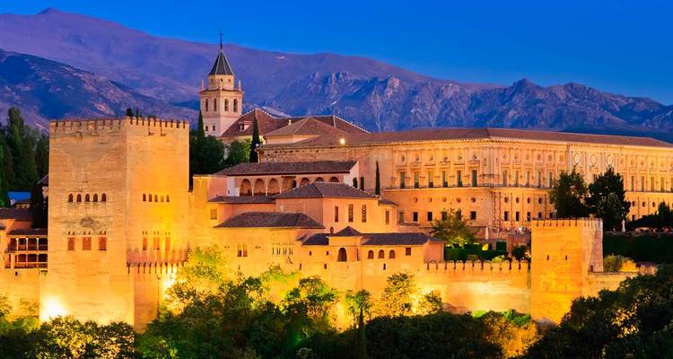 Illuminated Alhambra in Granada with mountains in the background.