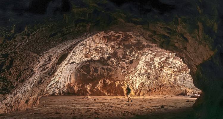 Person standing inside a large cave with dramatic lighting.