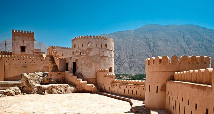 Forteresse avec tours circulaires sur fond de montagne.