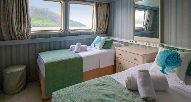 Cabine de bateau de croisière avec lits et fenêtres donnant sur la vue océanique.