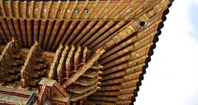 Aleros pintados con detallados dancheong de un templo coreano contra un cielo blanco