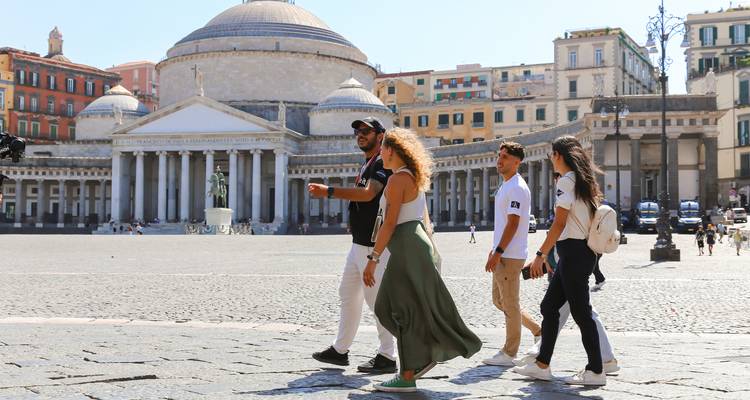 Group of people walking in a plaza with historic architecture.