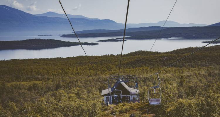 Télésiège au-dessus d'un paysage luxuriant avec un lac et des montagnes.