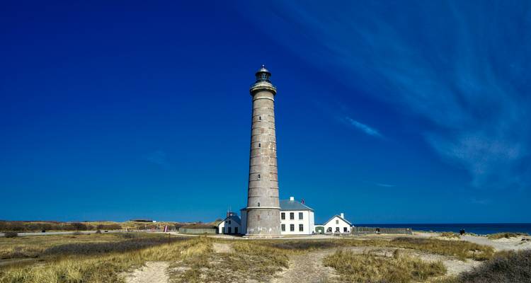 Tall lighthouse on a sandy beach with clear sky.