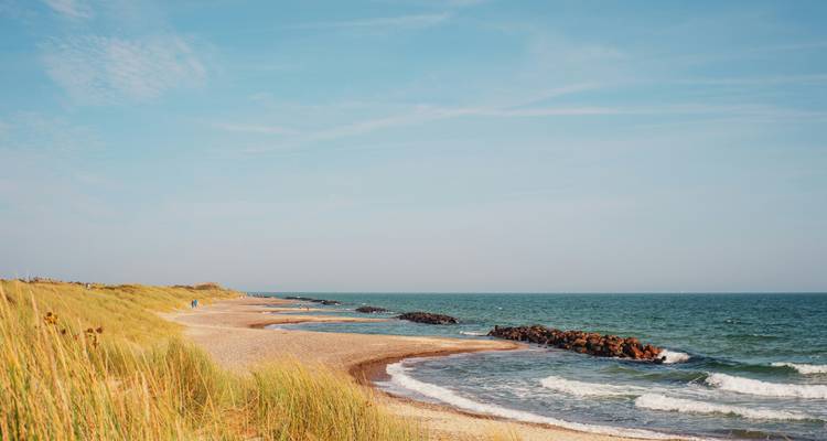 Peaceful sandy beach with gentle waves and a blue sky.