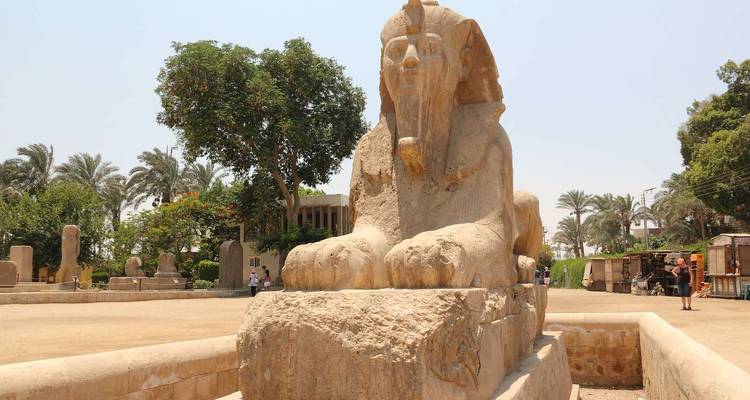 Statue of a sphinx in an outdoor area with trees.