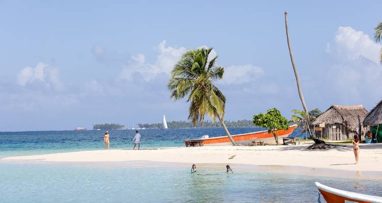 Plage tropicale avec des palmiers, des gens qui nagent et un bateau.