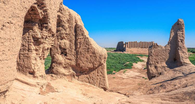 Ruines anciennes avec un grand mur de pierre et paysage désertique.
