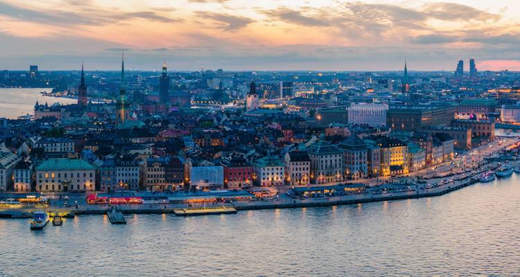 Cityscape view at sunset with a waterfront and buildings lighting up.
