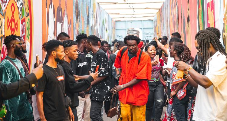 A lively group of people dancing and socializing in a colorful alley enclosed by art-covered walls.