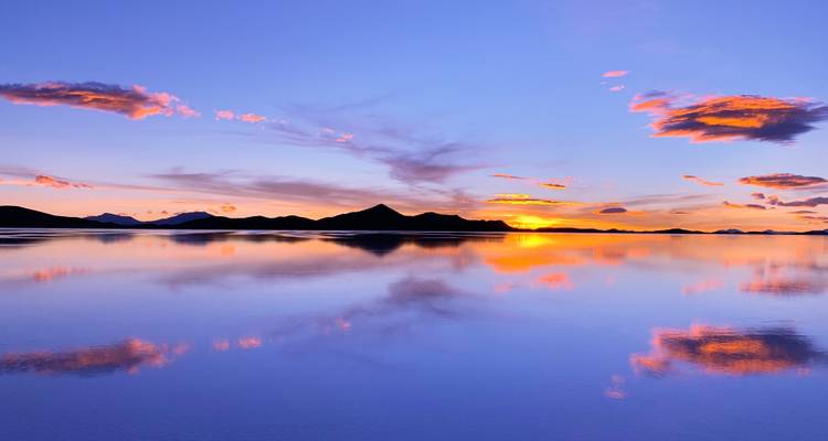 Zonsondergang over een reflecterende zoutvlakte met bergen in silhouet.