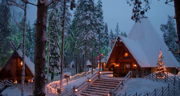 Cabane enneigée éclairée au crépuscule entourée d'arbres couverts de neige et de clôtures en bois.