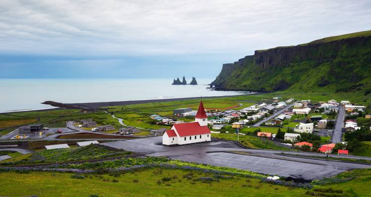 Village avec église au toit rouge et vue sur l'océan à Vik.