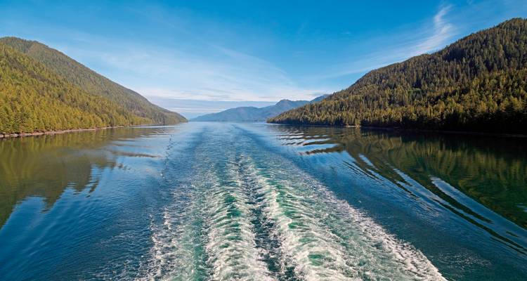 Une vue depuis un bateau ou un navire montrant le sillage dans l'eau, avec des collines de chaque côté.
