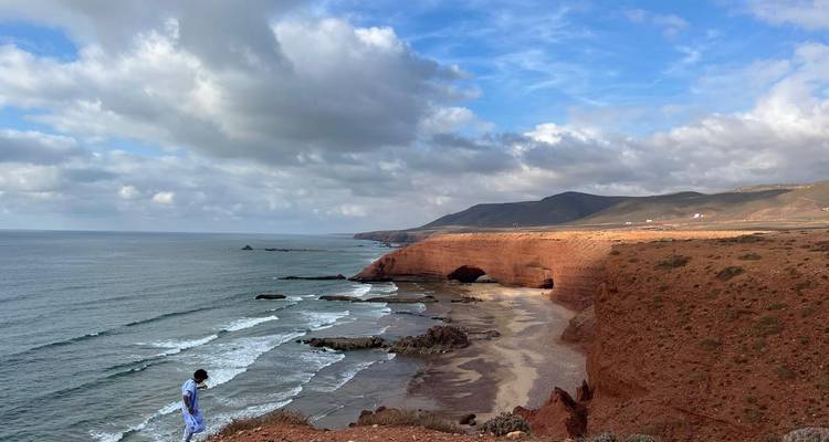 Une personne regardant au loin par-dessus des falaises et l'océan avec des arches à l'horizon.