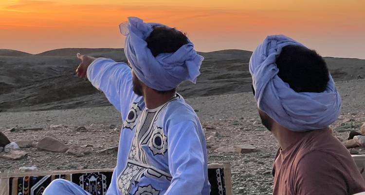 Deux personnes en tenue traditionnelle regardant un coucher de soleil sur le désert.