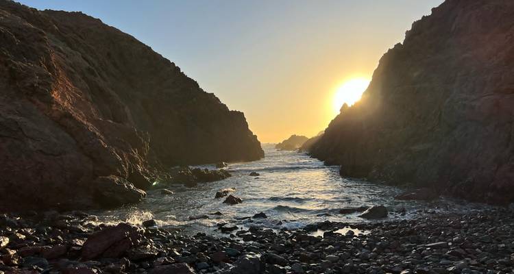 Une vue sur l'océan ensoleillée encadrée par des falaises rocheuses.