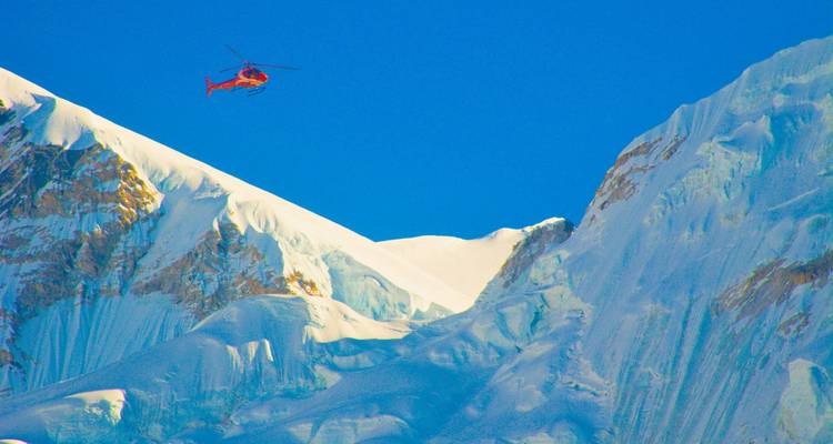 Helicopter flying near snow-covered mountains.