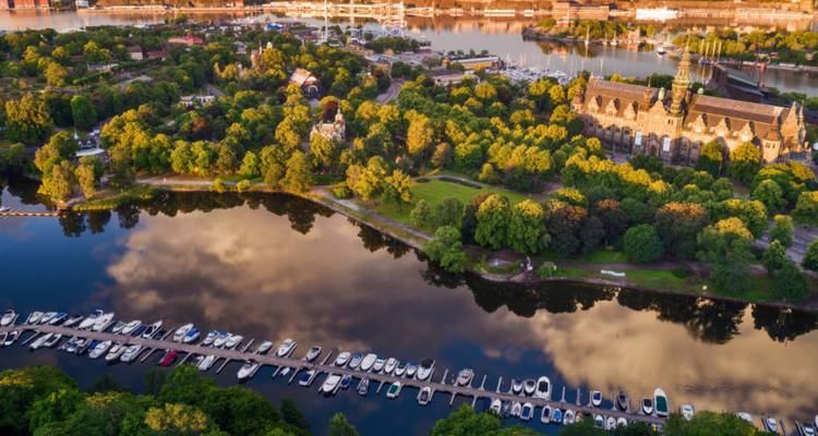Vue aérienne d'un parc avec un lac et un bâtiment historique, entouré de verdure.