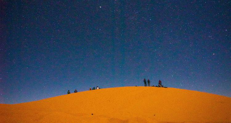 Ciel étoilé nocturne au-dessus de dunes de sable avec des silhouettes.