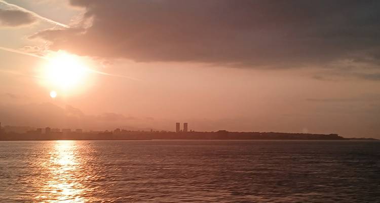 Sonnenuntergang über einem Meer mit einer Stadt im Hintergrund.