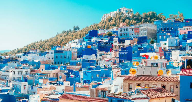 Vue panoramique de la colline de Chefchaouen avec ses maisons bleues et blanches sous un ciel dégagé.