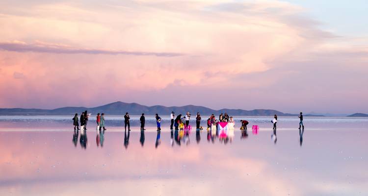 People walking on the mirrored surface of the Uyuni Salt Flats at sunset.