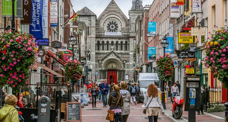 Belebte Fußgängerzone in Dublin mit Geschäften, Cafés und hängenden Blumen.