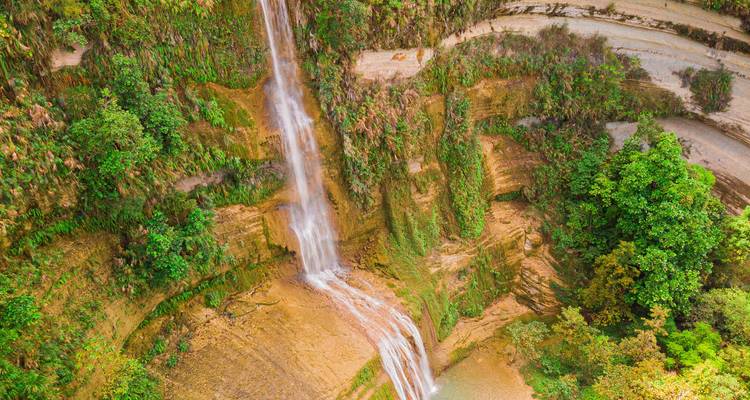 Wasserfall, der eine felsige Klippe hinunterstürzt, umgeben von Grün.