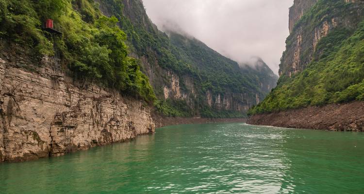 Steile grüne Schlucht mit türkisfarbenem Fluss, der sich zwischen nebelbedeckten Klippen hindurchwindet.