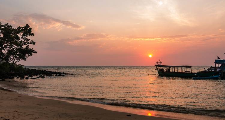 Sonnenuntergang über einem ruhigen Strand mit Booten.