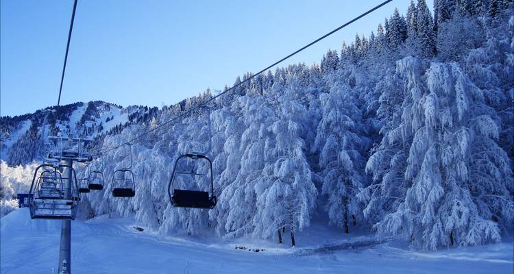 Ski lift with snow-covered trees and mountains.