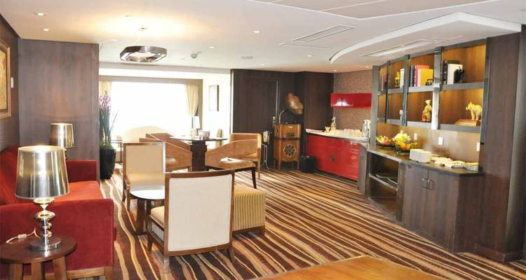 Salón de suite de crucero decorado con calidez, con alfombra a rayas y muebles clásicos.