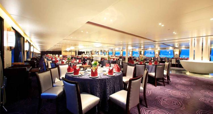 Elegante salón de comedor de crucero con mesas redondas, servilletas rojas dobladas y alfombra mullida.