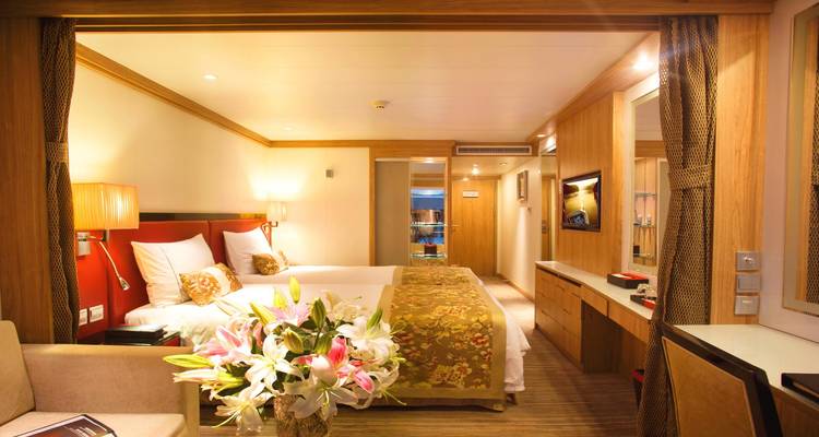 Camarote luminoso de crucero con cama doble, lirios frescos y paneles de madera cálida.