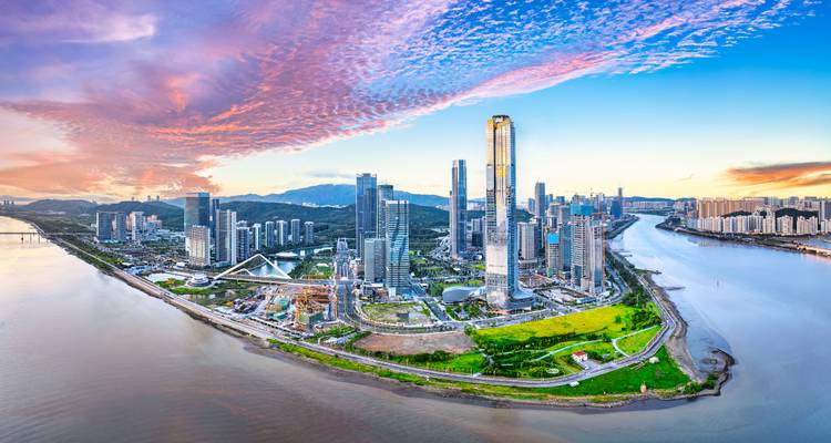 Vista aérea de una ciudad moderna en la orilla de un río con un cielo colorido.