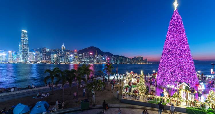 Un enorme árbol de Navidad rosa brilla en la bahía de Hong Kong con el horizonte de la ciudad al atardecer.