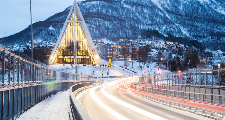 Pont menant à une église moderne avec des traînées lumineuses de voitures qui passent.