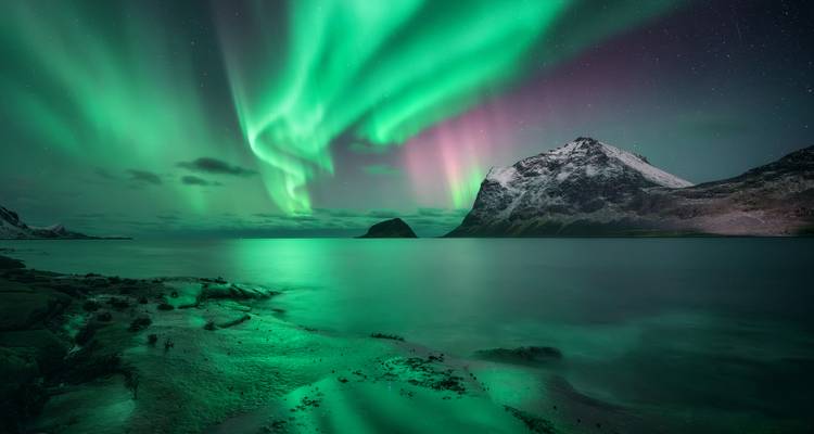 Aurores boréales au-dessus d'une montagne reflétées dans l'eau.