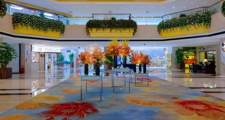 Helle, moderne Hotellobby mit farbenfrohen Blumenarrangements, gemustertem Teppich und glänzenden Böden