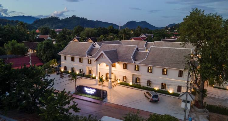 Evening aerial view of an elegant boutique hotel complex surrounded by tropical greenery and mountains.